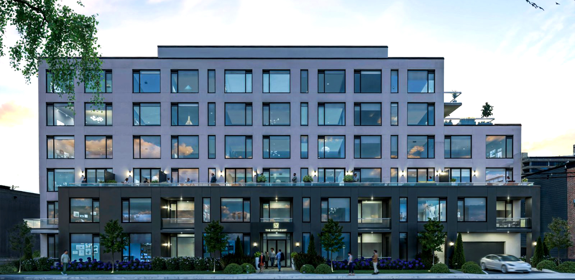 Modern multi-story apartment building with large windows, balconies, landscaping, and people outside at dusk.