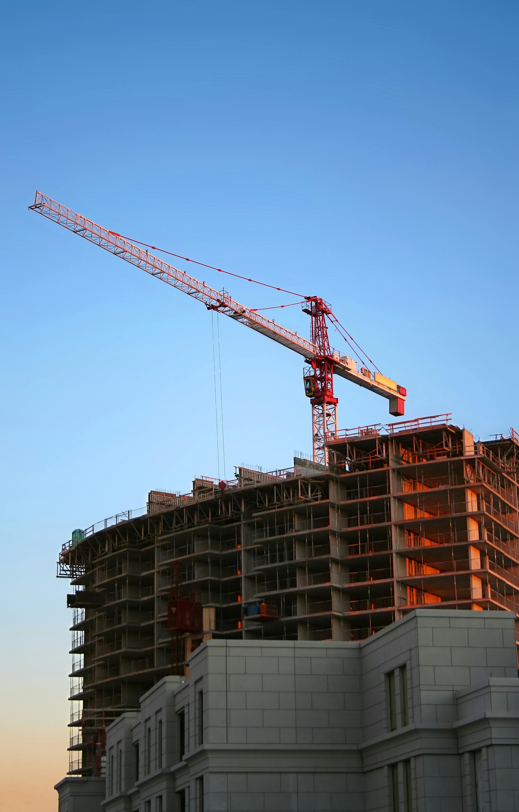 Construction crane above a partially built multi-story building at sunset.