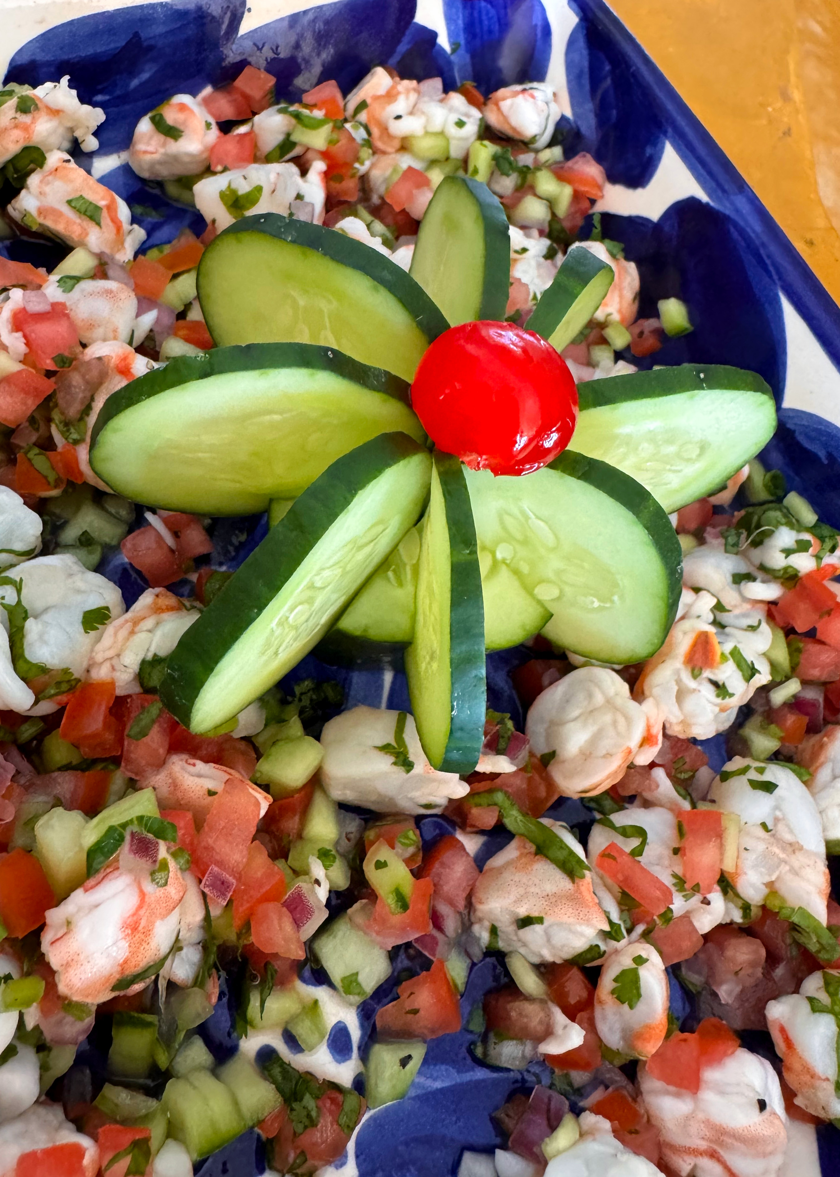 Fresh seafood ceviche with diced tomatoes, cucumber, herbs, and a cucumber flower garnish topped with a cherry tomato.