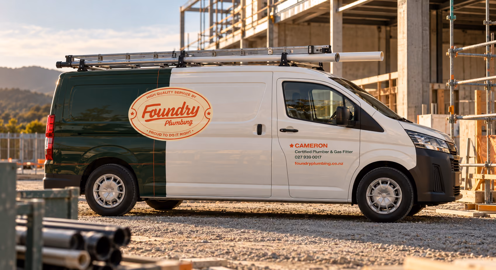 White and green Foundry Plumbing service van parked at a construction site with ladders and pipes on the roof and construction scaffolding in the background.