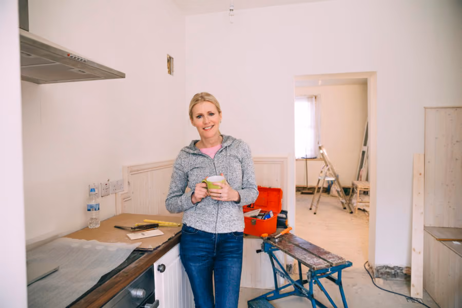 A woman holding a cup of coffee and standing by home renovation equipment. She can't afford to fix up her house.