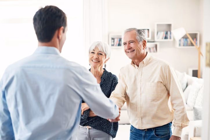 An older couple shaking hands with a house investor that buys houses for cash.