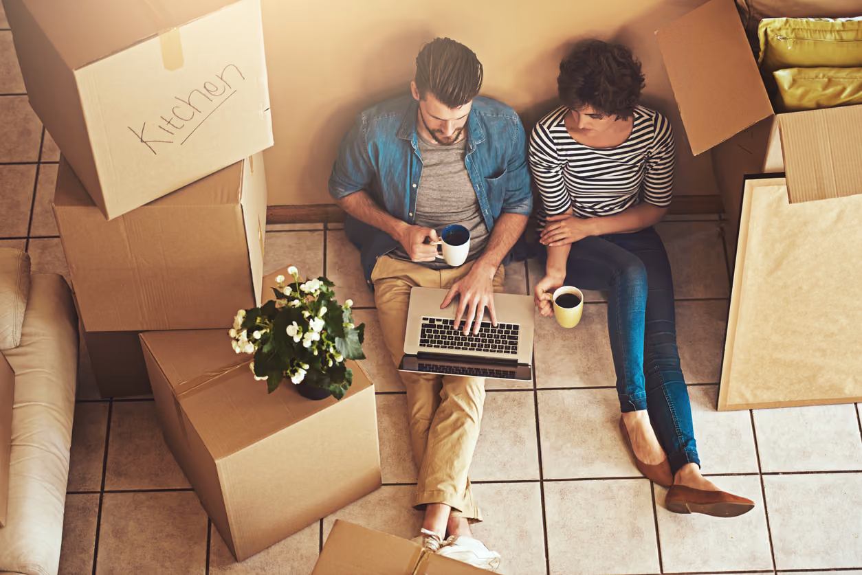 A couple sitting on the floor by moving boxes trying to figure out how to sell their home by owner.