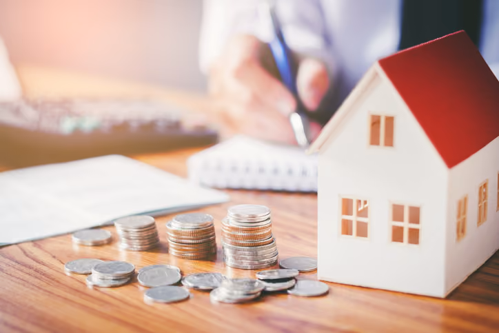 A model house with a stack of coins on a table, signifying tax implications when selling a rental property.