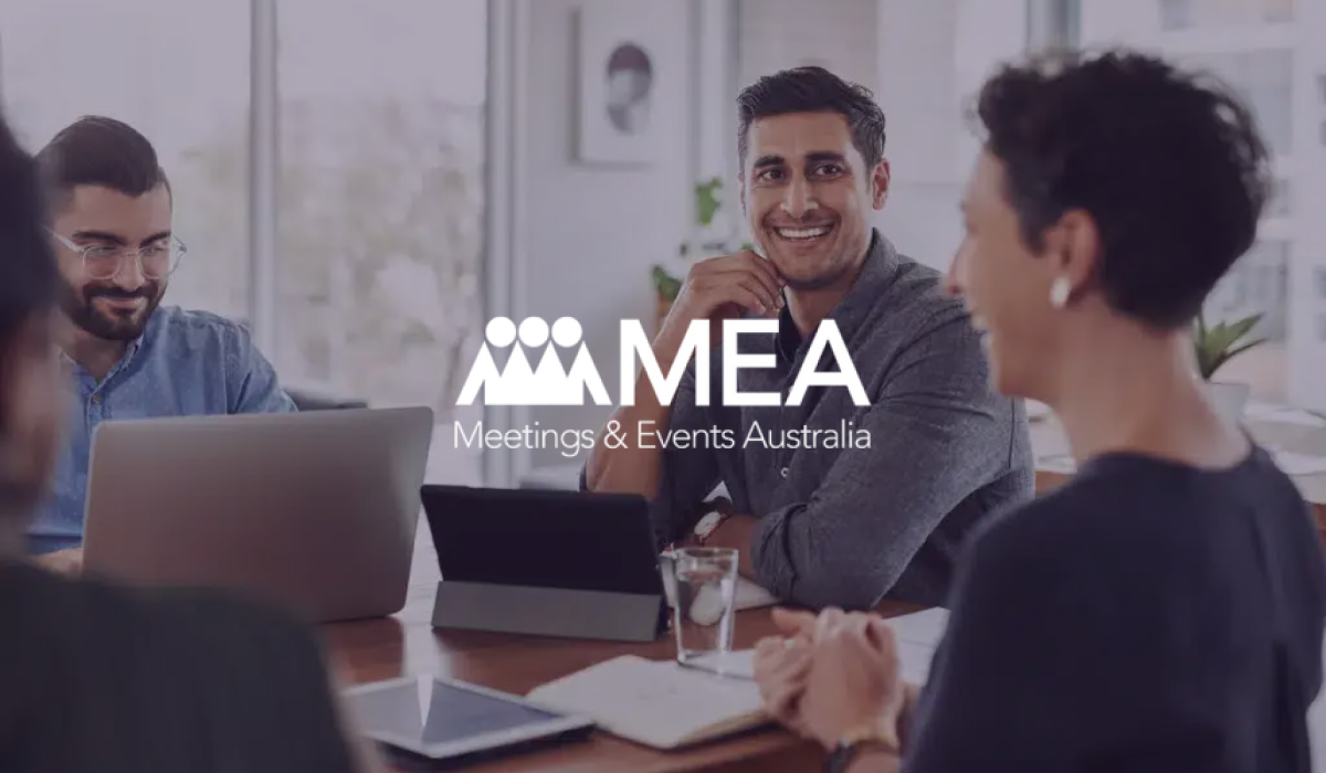 Meetings & Events Australia logo over colleagues talking around a table with laptops