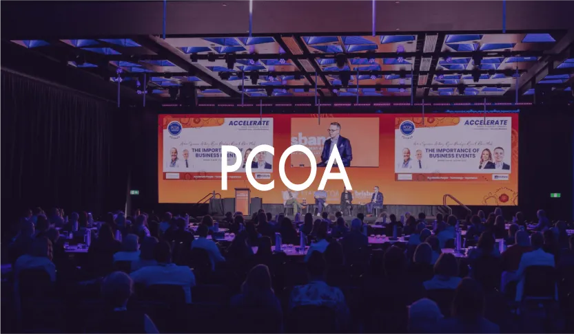PCOA logo over a conference panel session on stage in front of a seated audience