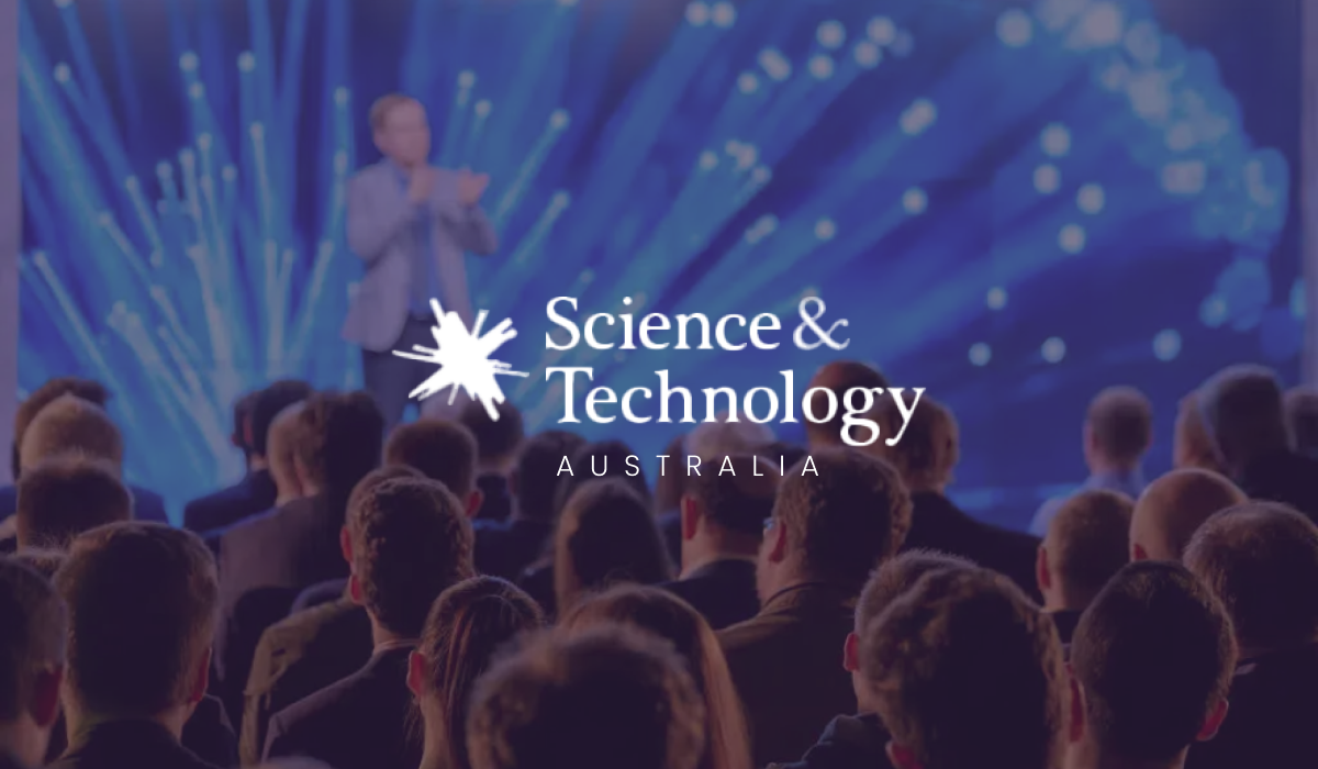 Science & Technology Australia logo over an audience watching a speaker on a blue-lit stage