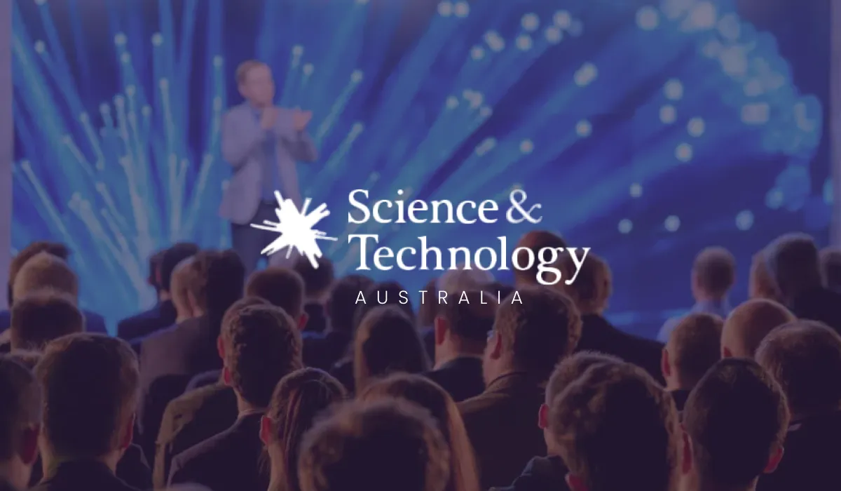 Science & Technology Australia logo over an audience watching a speaker on a blue-lit stage