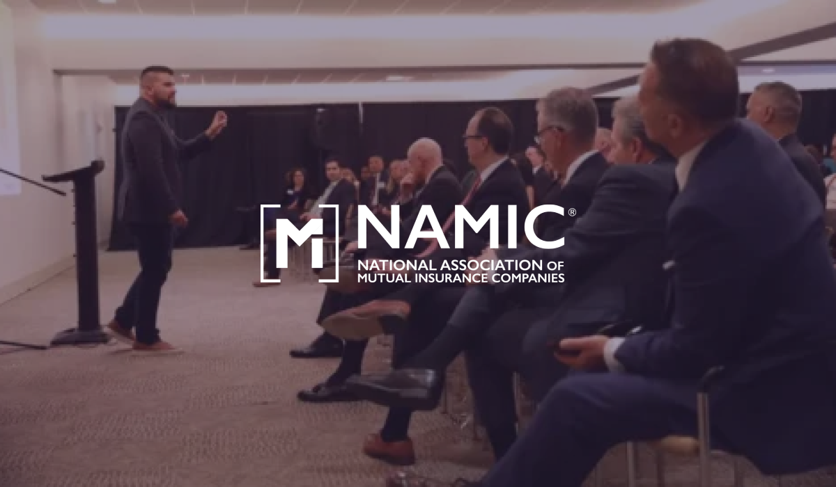 NAMIC logo over a speaker addressing a seated audience in business suits