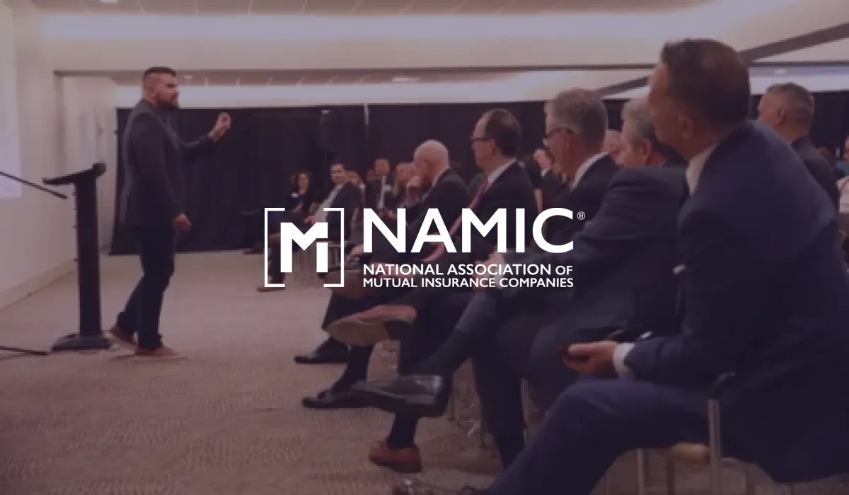 NAMIC logo over a speaker addressing a seated audience in business suits
