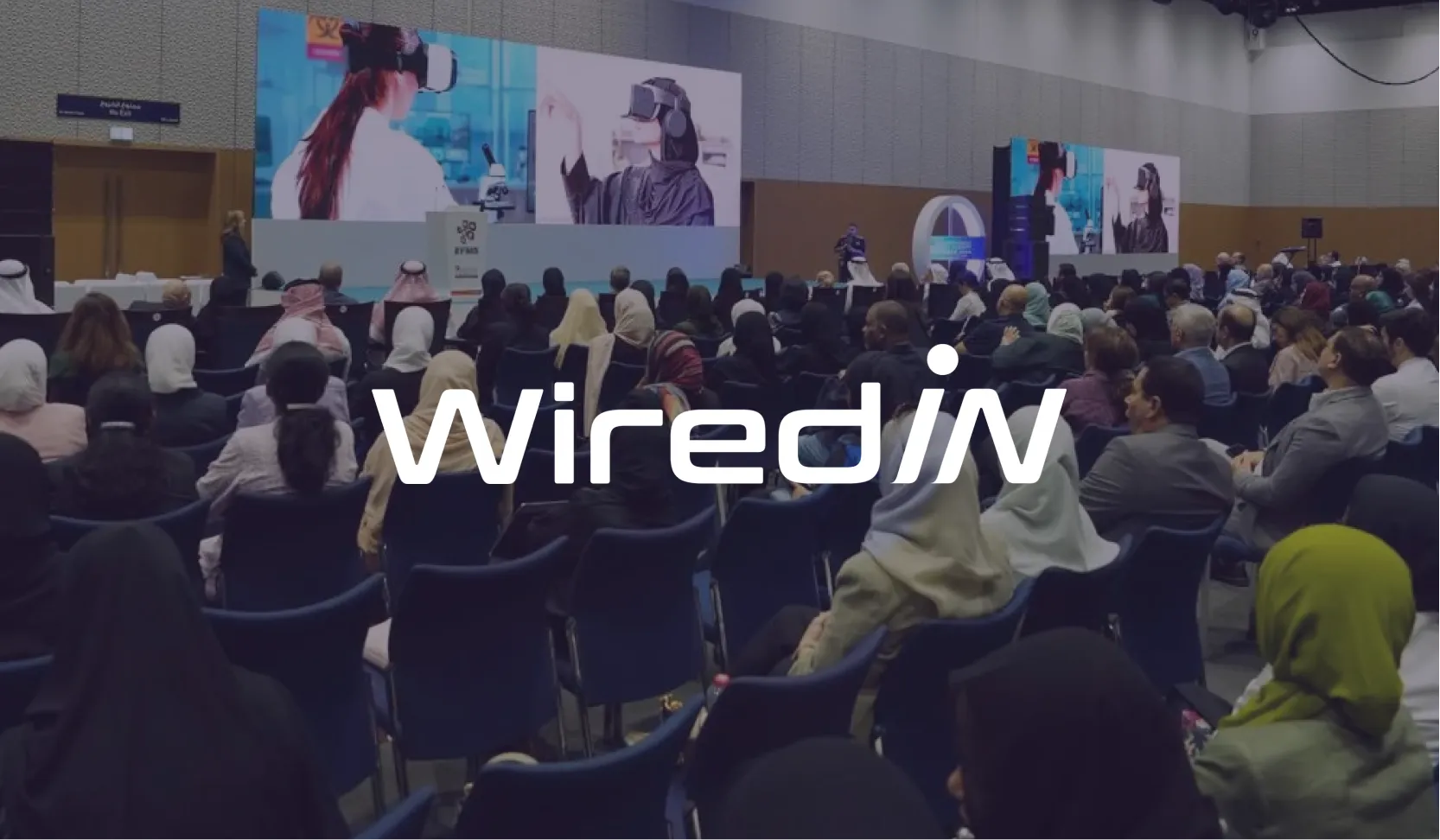 WiredIN logo over a packed conference hall audience watching a large screen