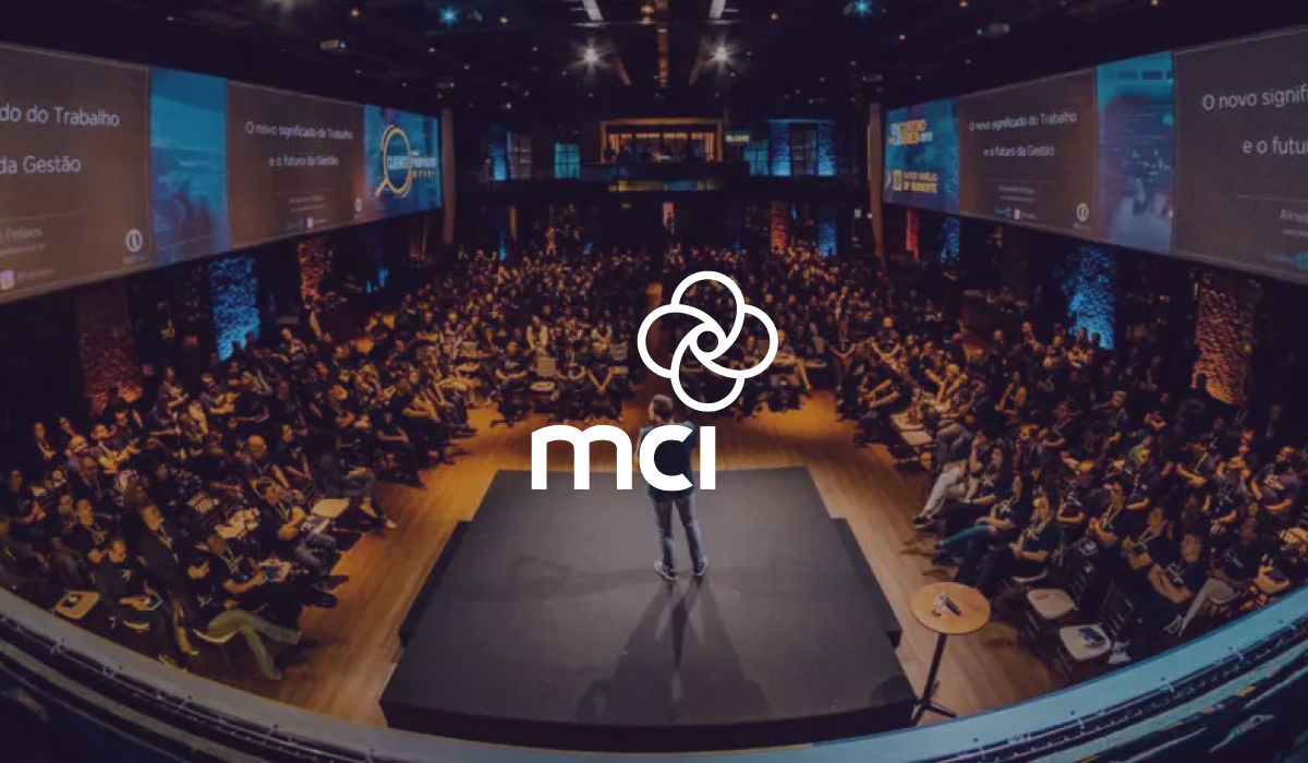 MCI logo over a speaker alone on stage in a theatre surrounded by a large audience