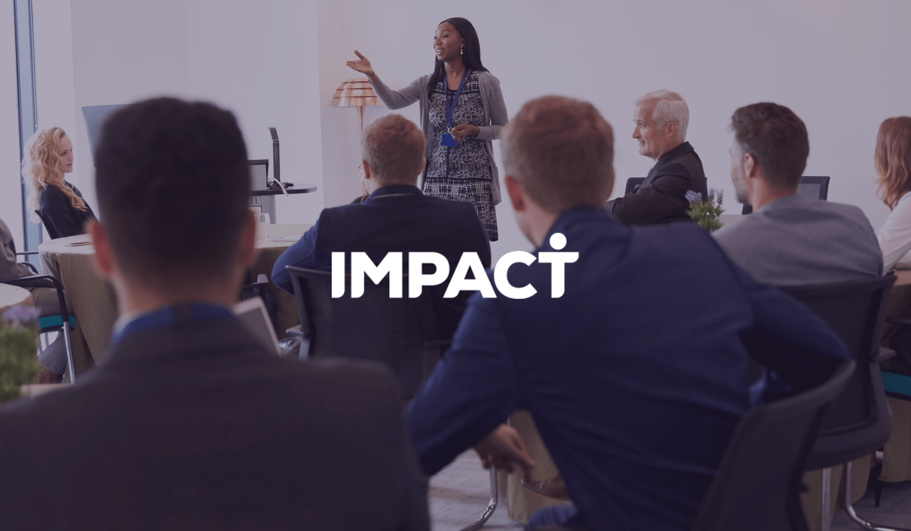 Impact logo over a woman presenting to a seated group in a bright meeting room