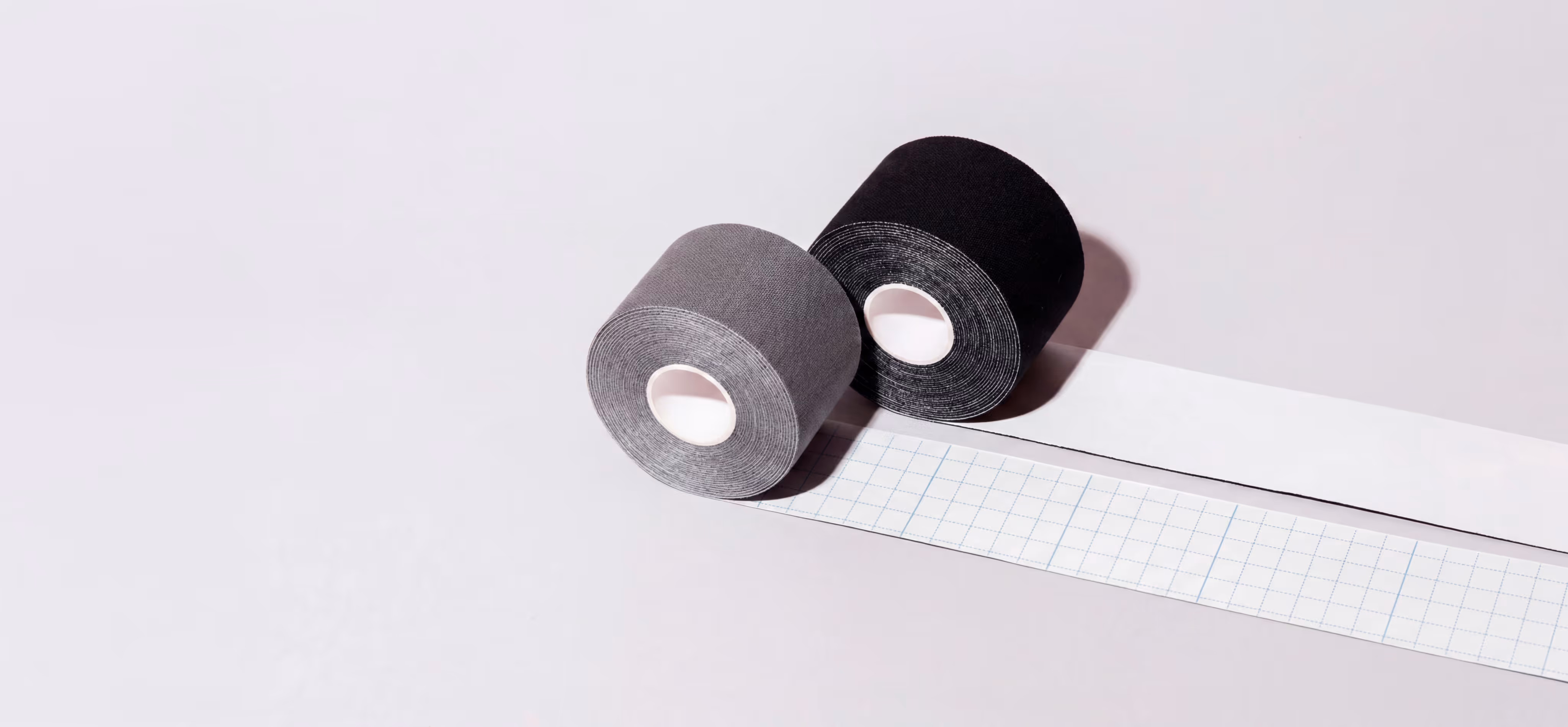 Zwei Rollen Klebeband, eine schwarz und eine grau, mit teilweise abgerolltem weißen Untergrund.