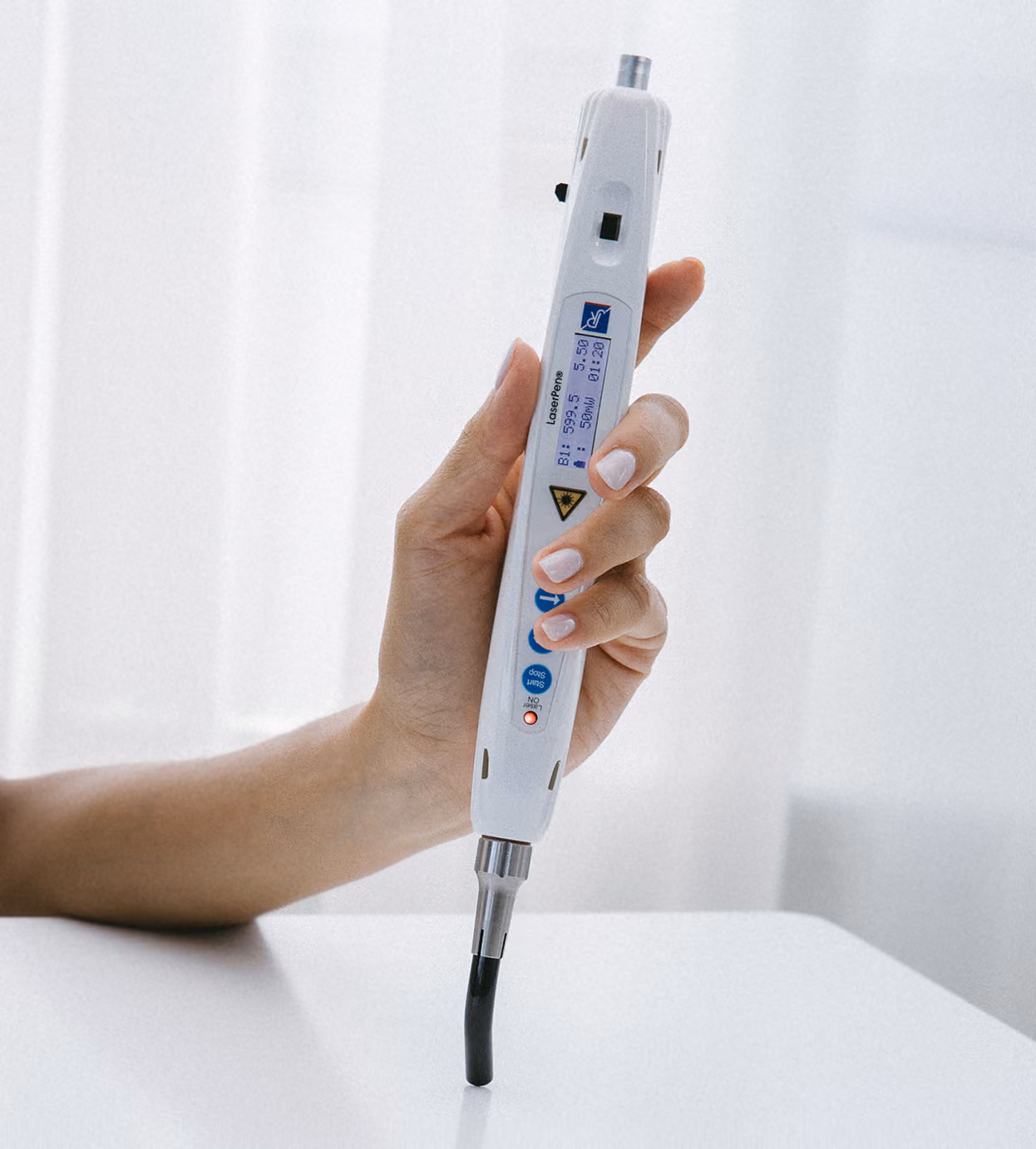 Hand hält ein weißes, elektronisches medizinisches Gerät mit digitaler Anzeige und mehreren Knöpfen, das auf einer weißen Oberfläche steht.