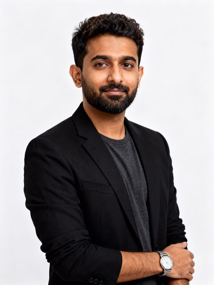 Confident man with beard wearing black blazer and gray shirt, arms crossed, against white background.