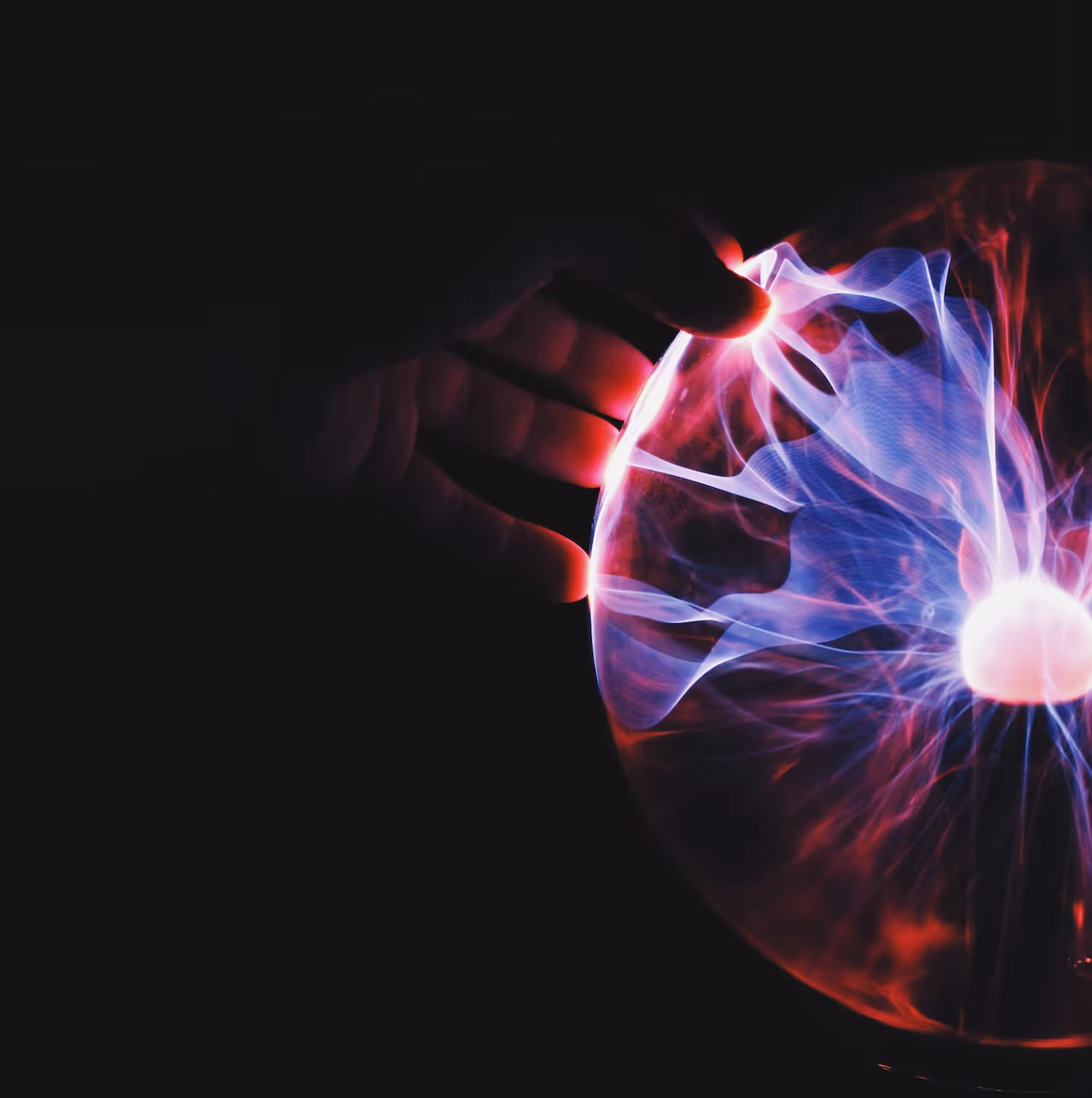 Hand touching a glowing plasma ball with red and blue electric streams inside a dark background.