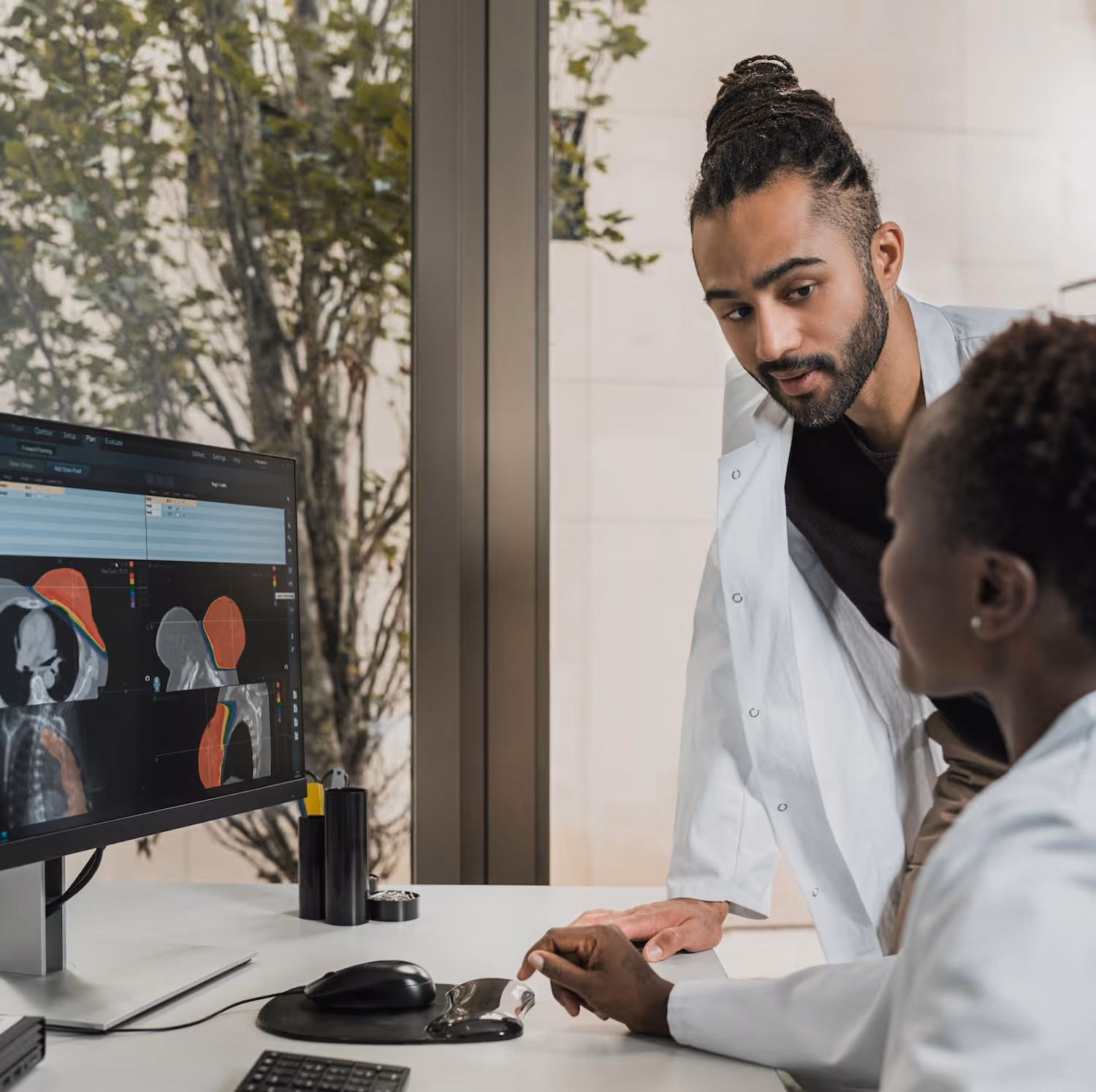 Two doctors in white coats studying medical images on a computer screen in an office.