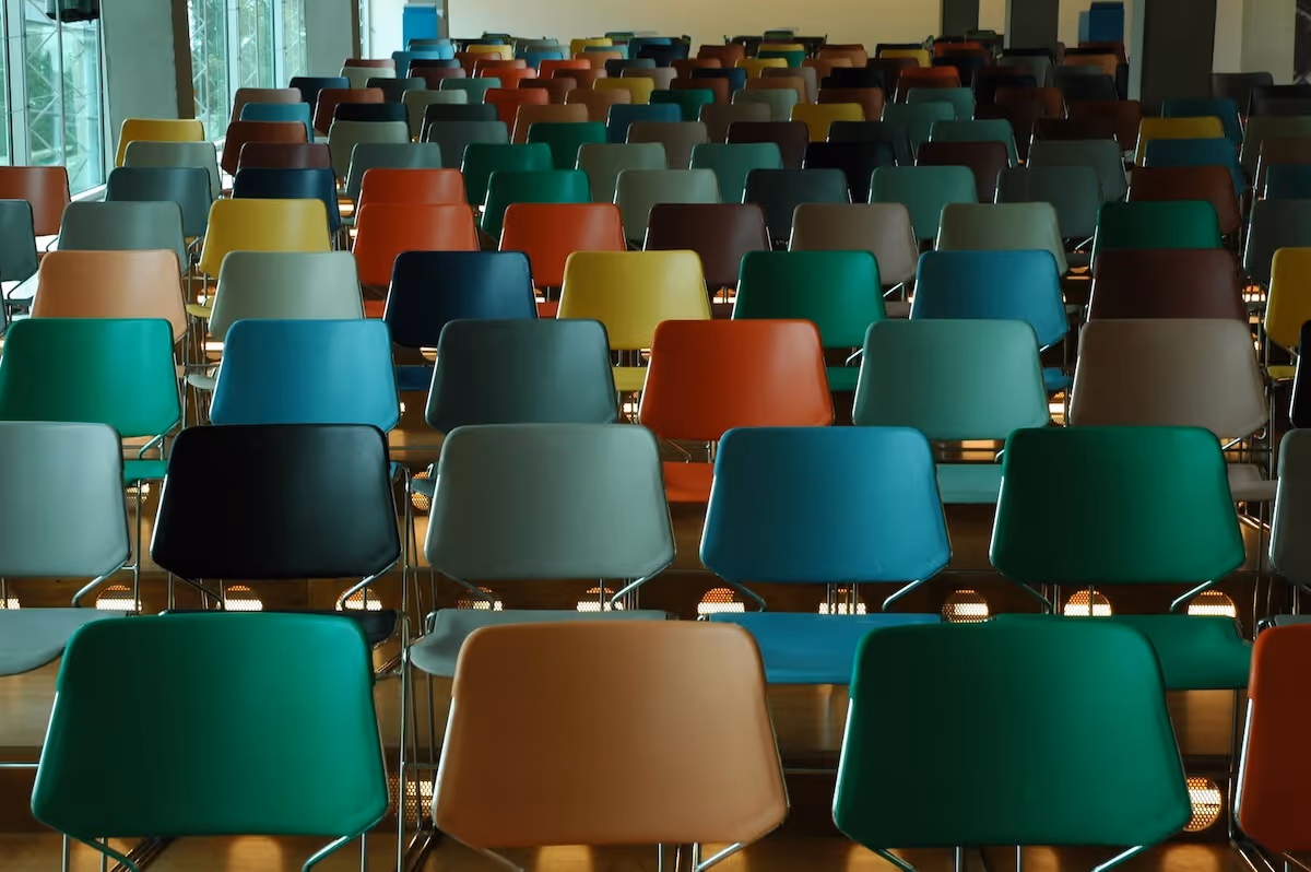 Rows of empty colorful chairs in a large room with windows on the left side.