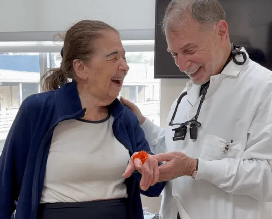 Smiling doctor showing an elderly woman a red item on her finger in a bright room.