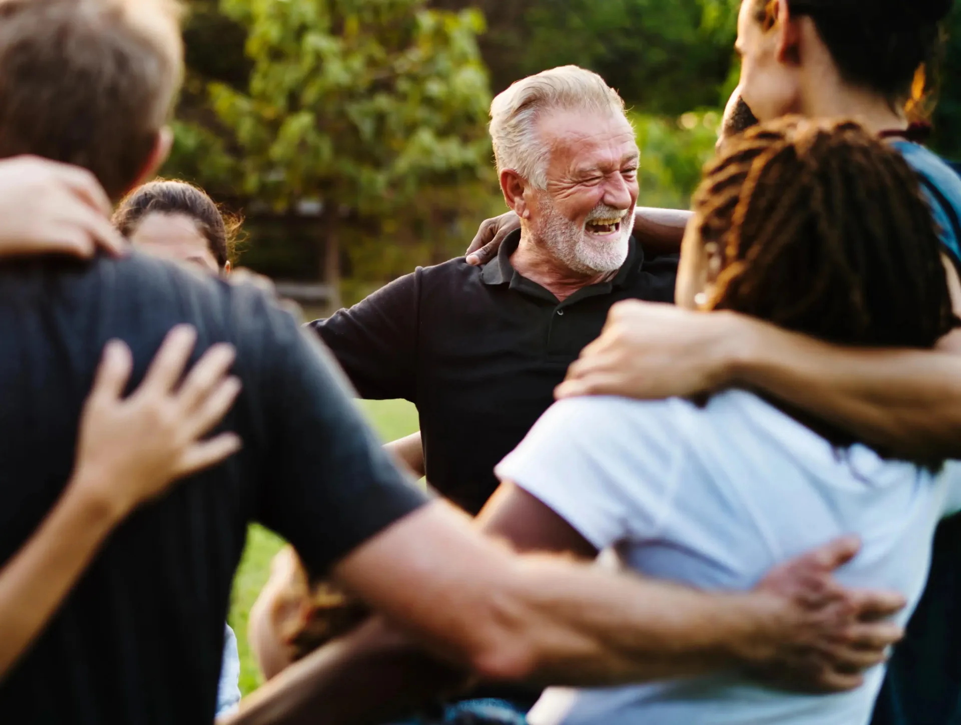 Diverse group of people standing close in a circle outdoors, smiling and embracing each other.