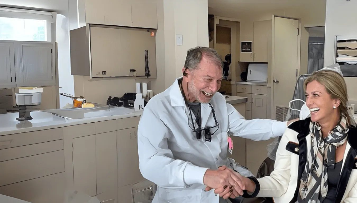 Smiling dentist shaking hands with a laughing female patient in a dental office.