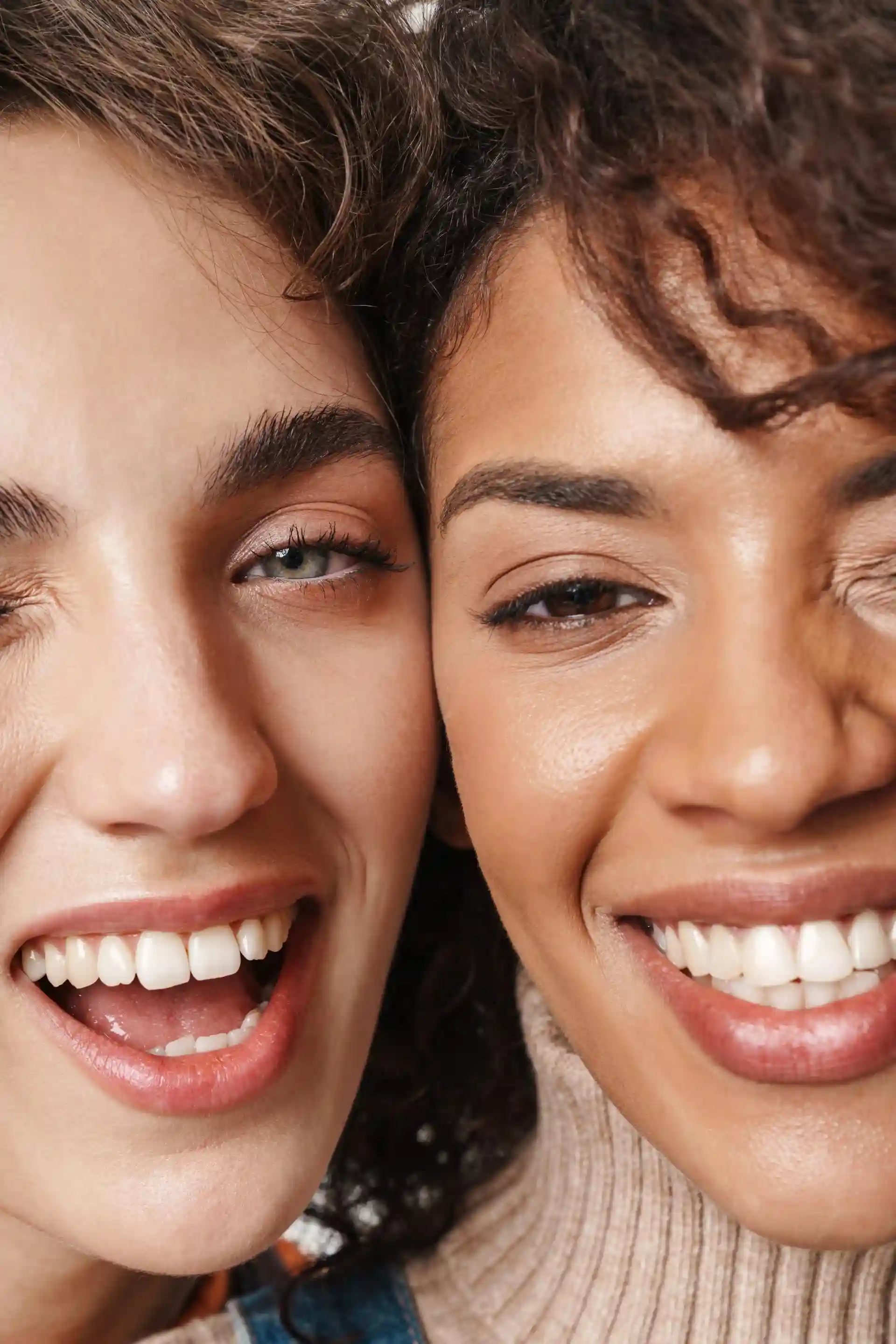 Close-up of two diverse women smiling and winking, showing white teeth and curly hair.