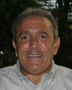 Smiling middle-aged man with short gray hair wearing a checkered shirt against a dark background.