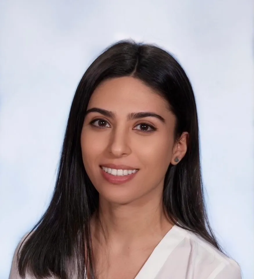 Smiling woman with long black hair wearing a white top against a light background.