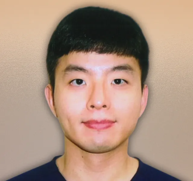 Portrait of an Asian man with short black hair wearing a dark top against a beige background.