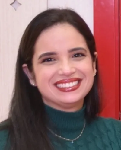 Smiling woman with long dark hair wearing a green turtleneck sweater and small earrings.