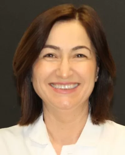Smiling woman with shoulder-length brown hair wearing a white shirt against a black background.