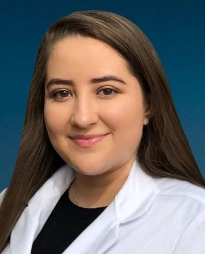 Woman with long brown hair wearing a white lab coat and black top against a blue background.