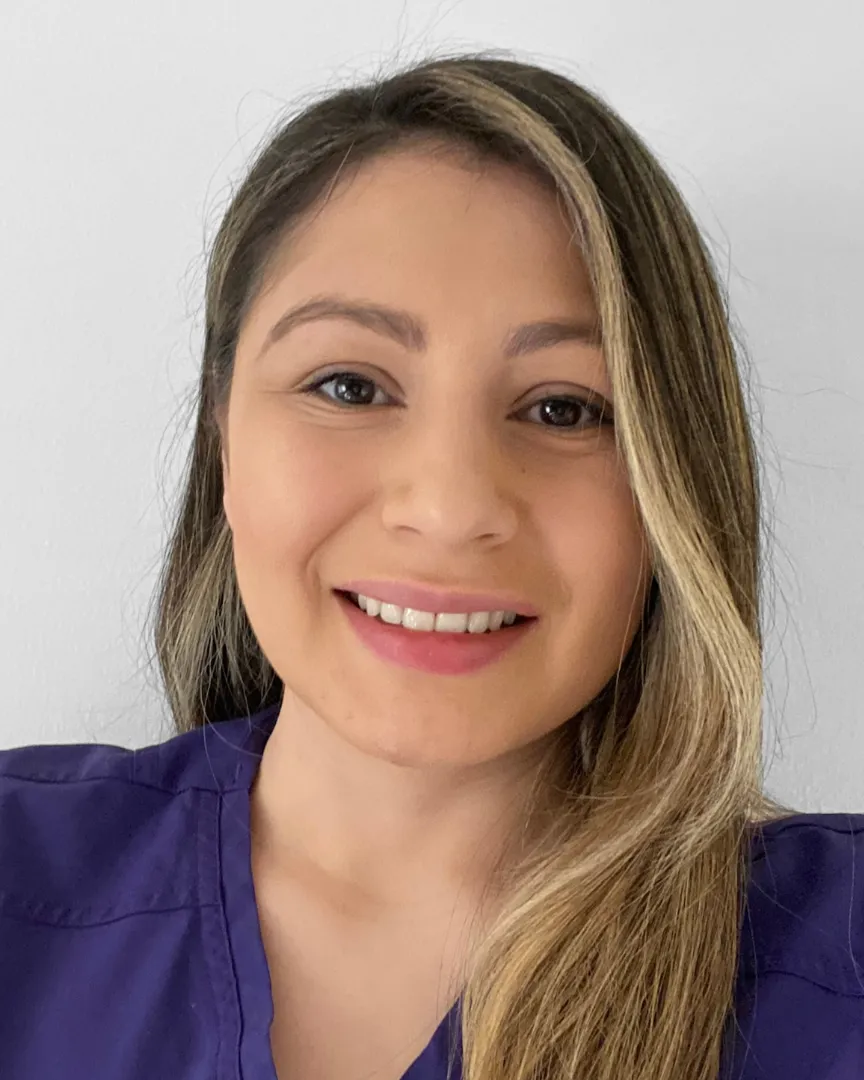 Smiling woman with light brown hair wearing a purple top against a white background.