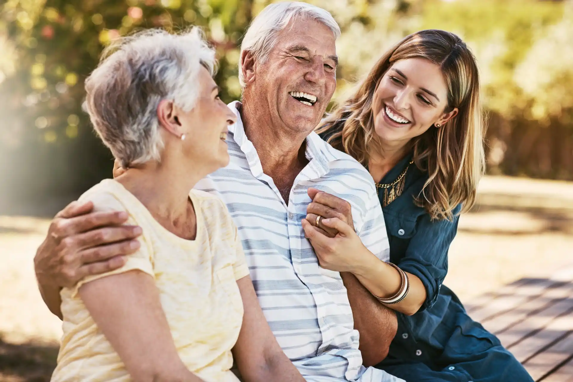 Three people smiling and sitting outdoors, sharing a joyful moment together on a sunny day.