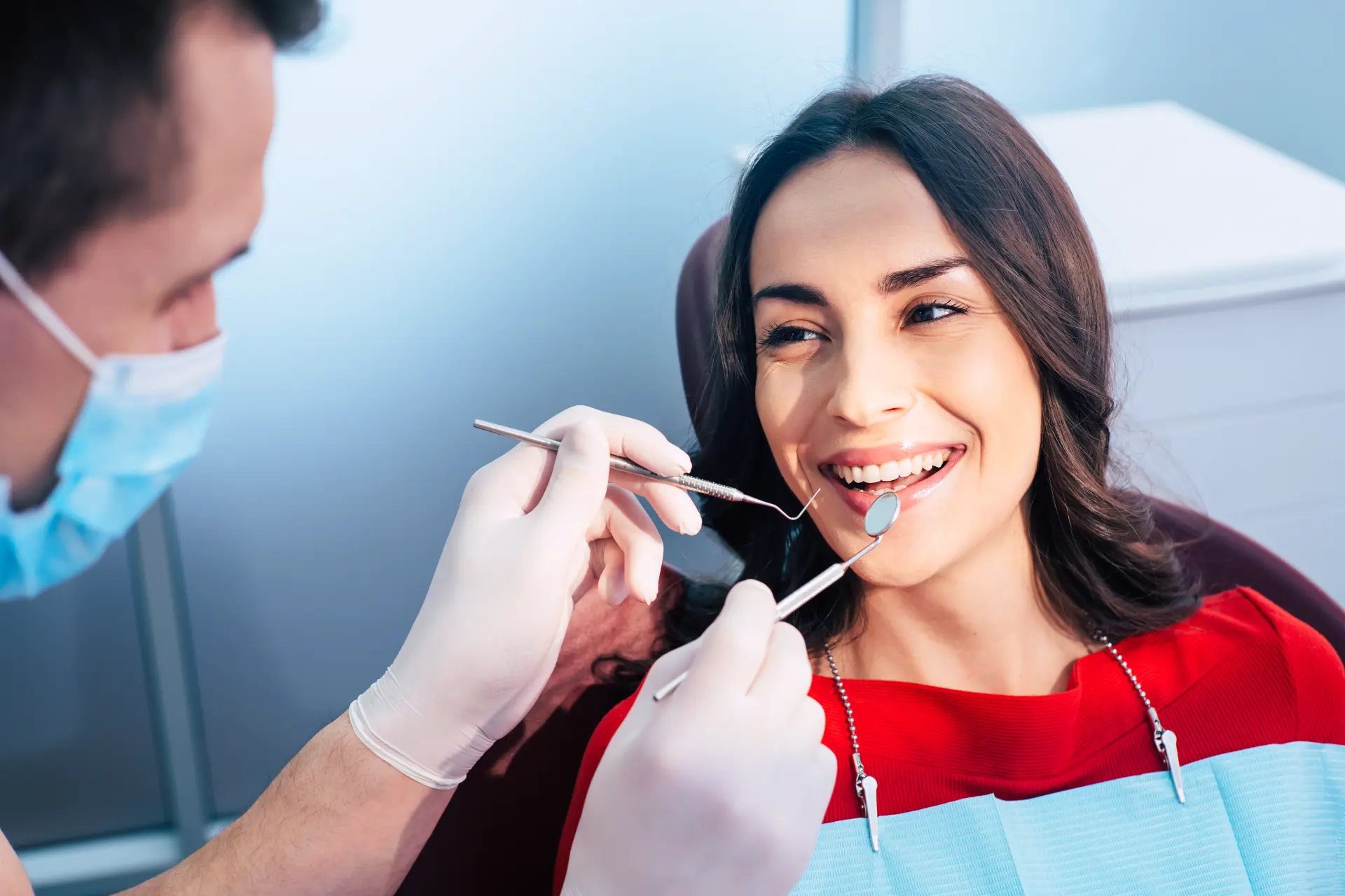 Dentist examining a smiling woman's teeth using dental tools during a checkup.