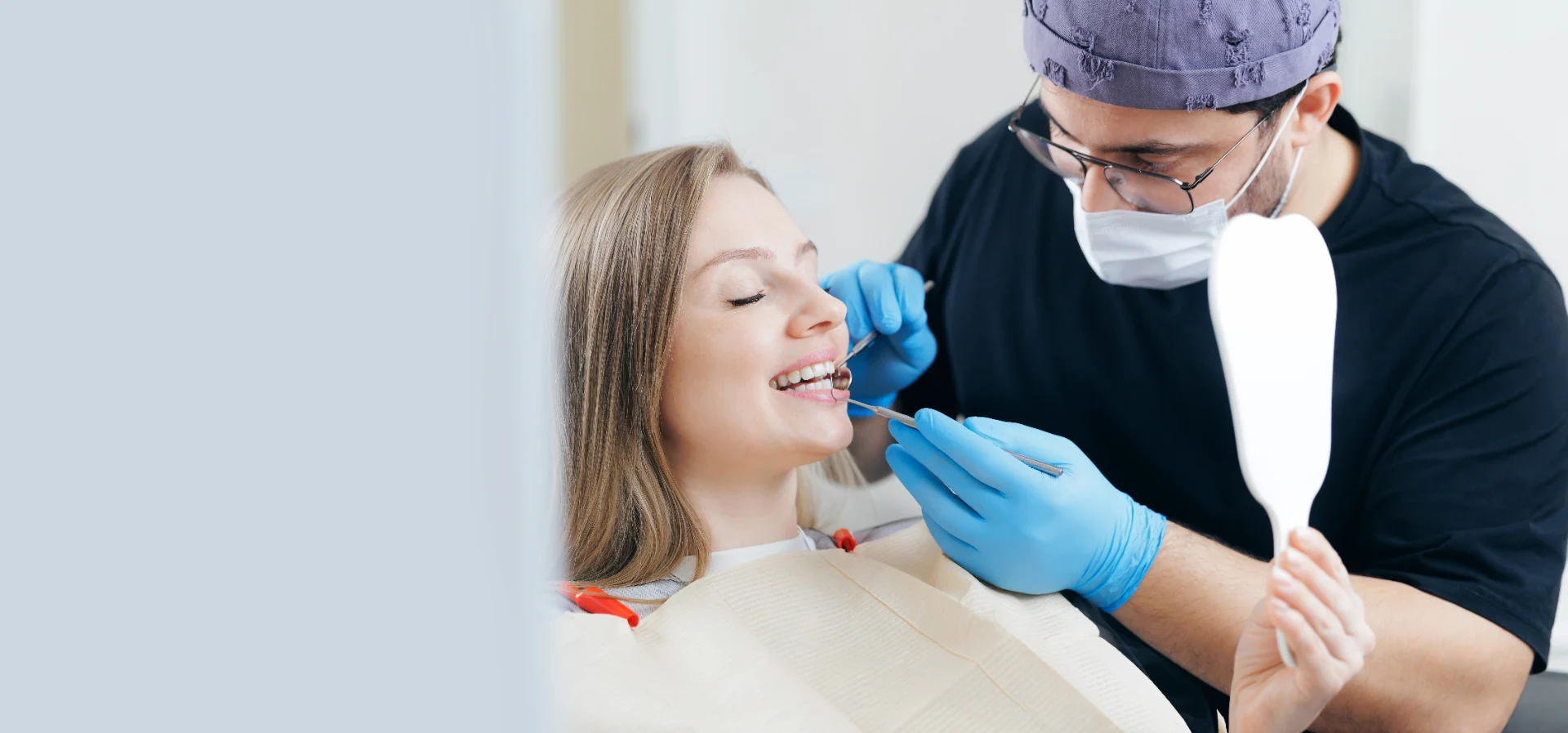 Female patient smiling while dentist with gloves examines her teeth using dental tools.