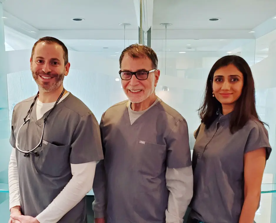 Three dental professionals in gray scrubs smiling in a modern dental office.