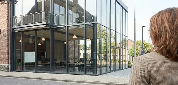 Personne regardant un bâtiment moderne avec de grandes fenêtres en verre et une salle de réunion visible.