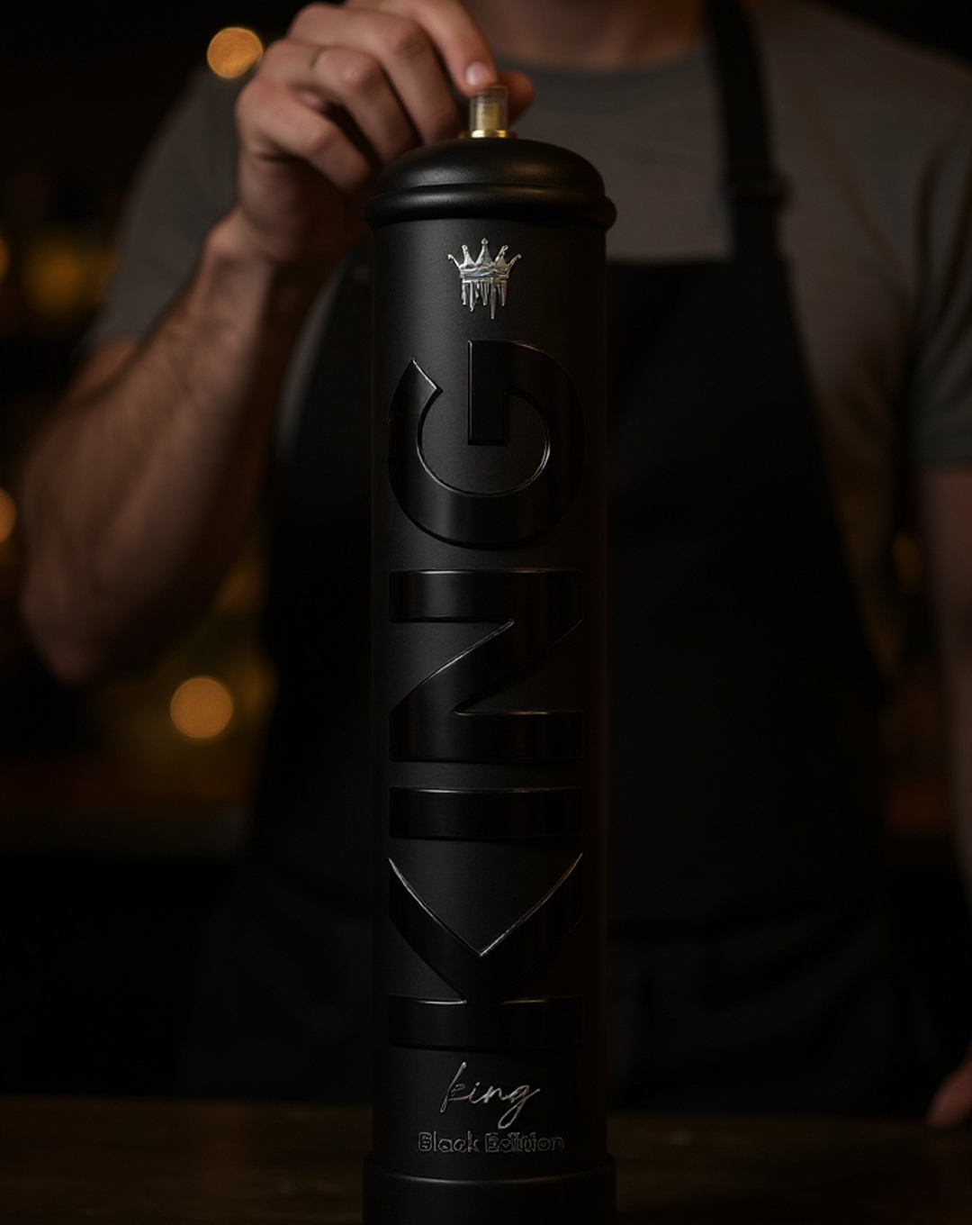 Close-up of a person holding a tall black cylindrical spray can labeled 'KING Black Edition' with a crown symbol above the text, against a dim background.