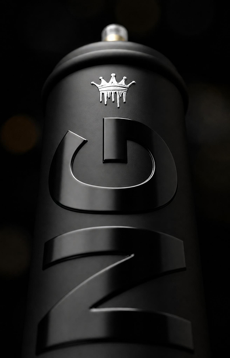 Close-up of a black aerosol spray can with embossed 'GZ' lettering and a small silver dripping crown logo above it, set against a dark background.