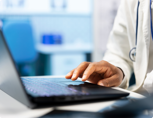 Doctor's hand typing on a laptop keyboard in a clinical office setting.
