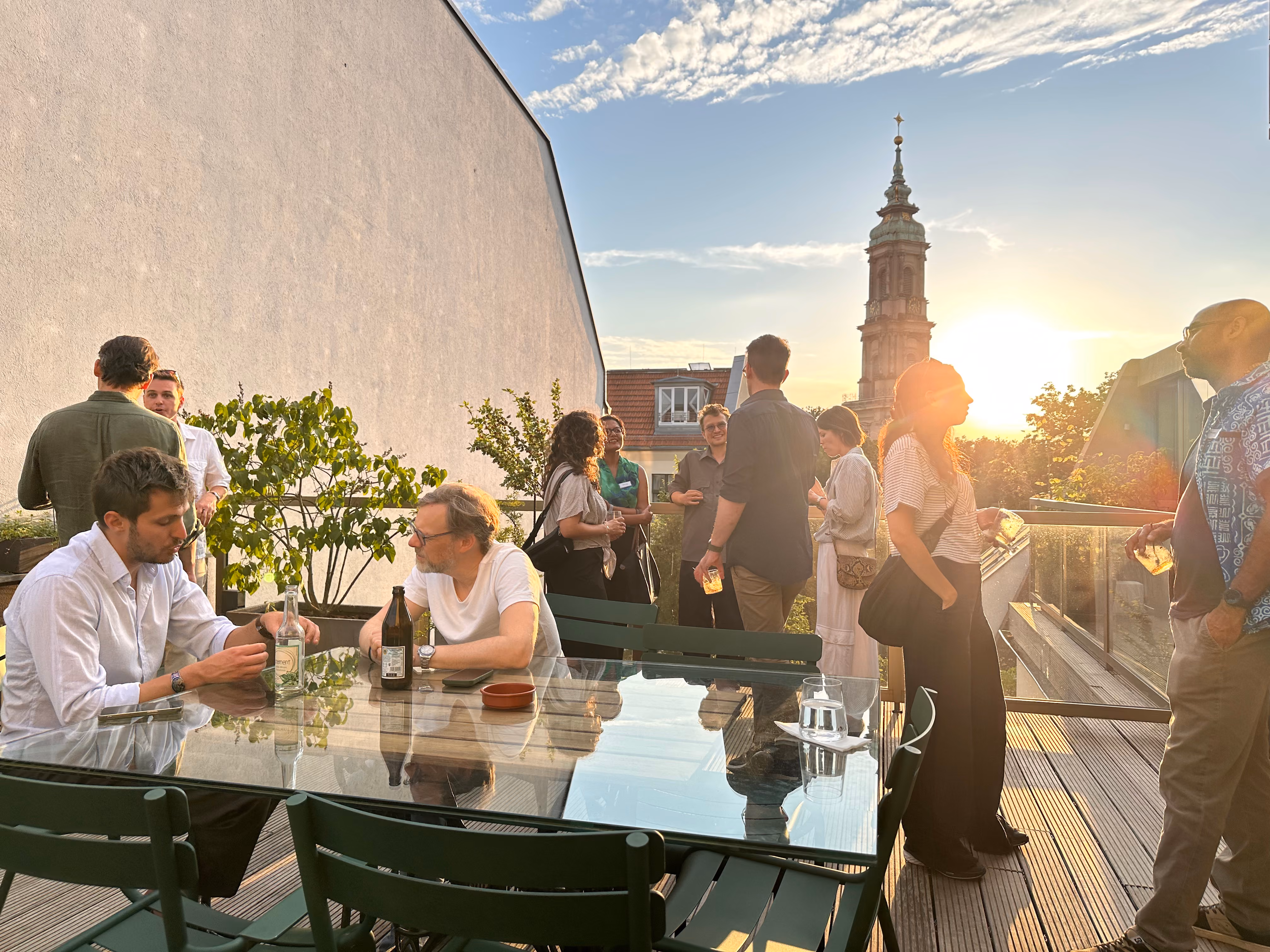 Group of people socializing on a rooftop patio at sunset with drinks and city views.