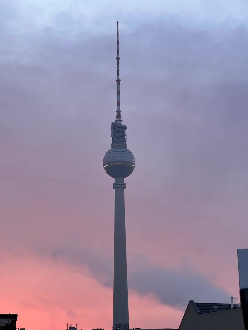Tall Berlin TV tower with antenna against a pink and purple sunset sky.