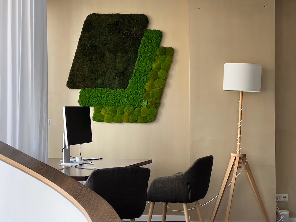 Modern office corner with black chairs, desk, computer monitor, wooden tripod lamp, and green wall art.