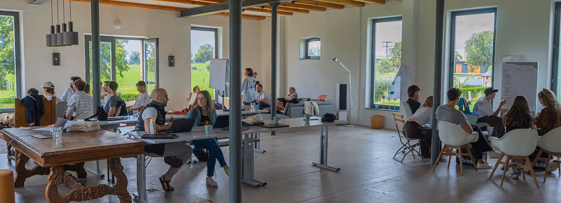 People collaborating and discussing in a bright, open workspace with large windows and wooden beams.
