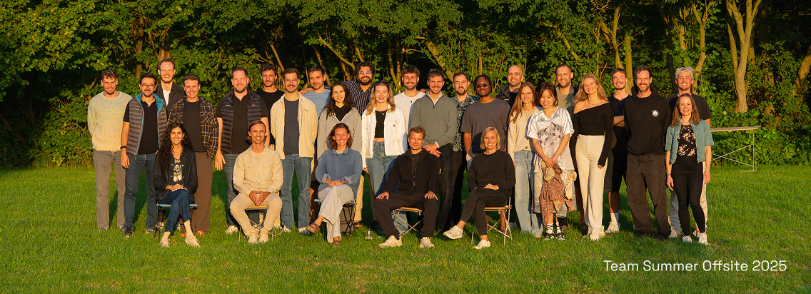Group photo of 30 people standing and sitting on grass with trees in background at a summer offsite.