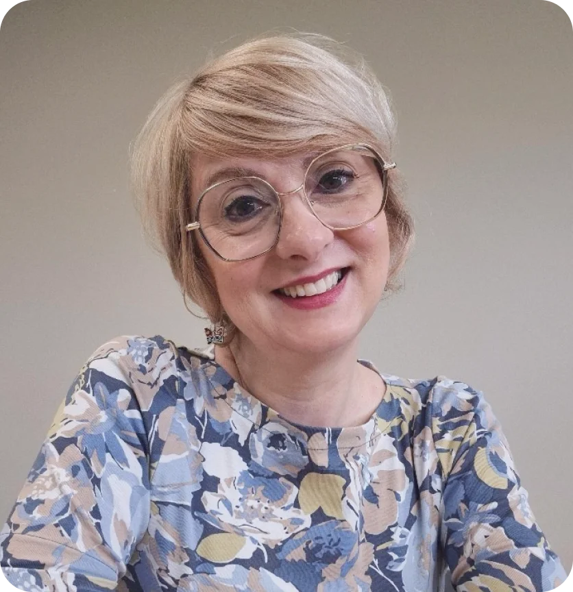 Smiling woman with short blonde hair and glasses wearing a floral blue and beige top.