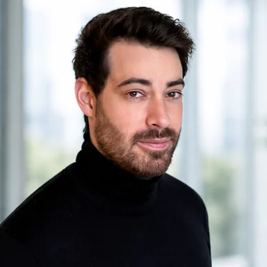 Man with dark hair and beard wearing a black turtleneck sweater, looking slightly to the side.