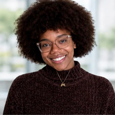 Smiling woman with curly hair and glasses wearing a dark sweater and a necklace with a crescent pendant.